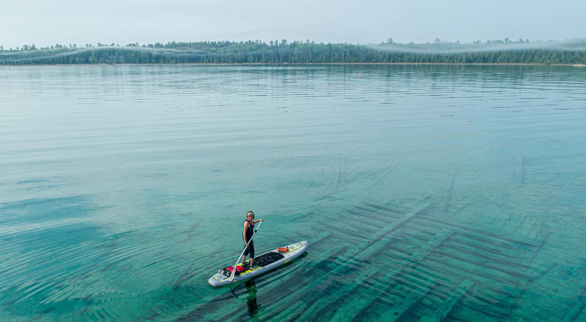 A person standing on a canoe on an expanse of turquoise water.