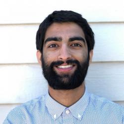 Mahtab Brar smiles in front of a background of white siding.