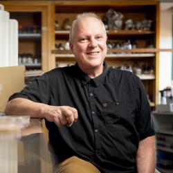 A man sits in a research laboratory with one arm on the benchtop.