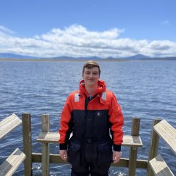 A man stands on a boat in a safety suit.