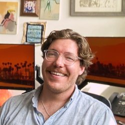 A man sits in an office with computer screens behind him.