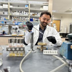 A man in lab coat and gloves uses a pipet.