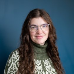 Headshot of a woman in a green fish sweater with long brown hair.