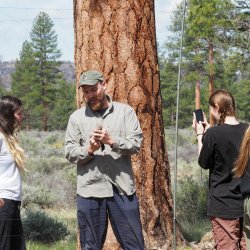 A man holds a bird and shows student. Background is trees and grass.