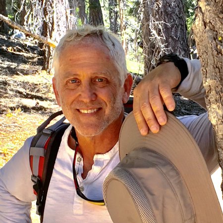 Portrait of Matthew Foreman leaning against a tree trunk in a forest background