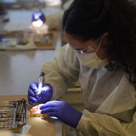 Ella Bailey wearing gloves and a mask, working with a teeth model, in a dental simulation lab at the OHSU Summit Program.
