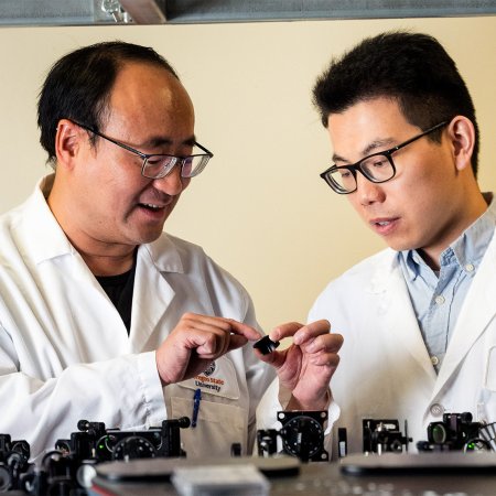 Two male scientists in lab coats work with a lasers.