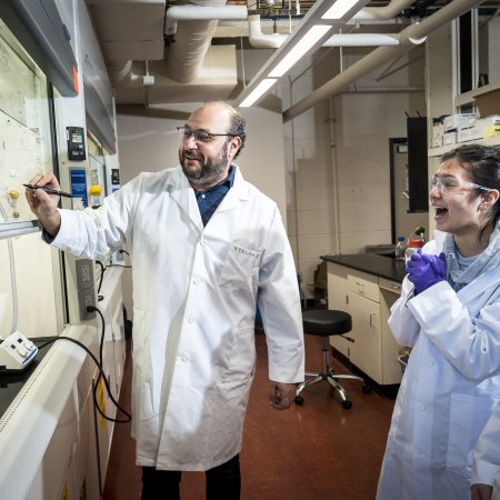 A man in a lab coat works with two students.