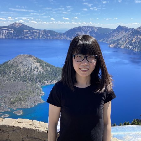 A woman in a black shirt poses for a photo in front of a stunning blue mountain lake.