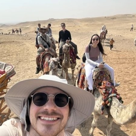A man in a hat poses while riding a camel.