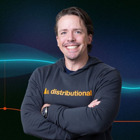 A man in a sweatshirt stands in front of a blue background.