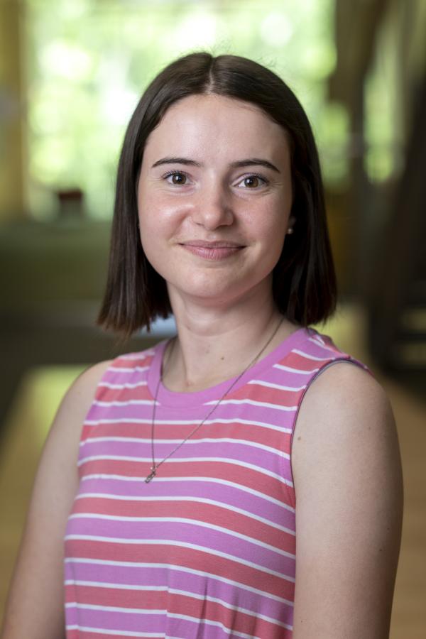 A woman with short brown hair stands for a headshot wearing a striped dress.