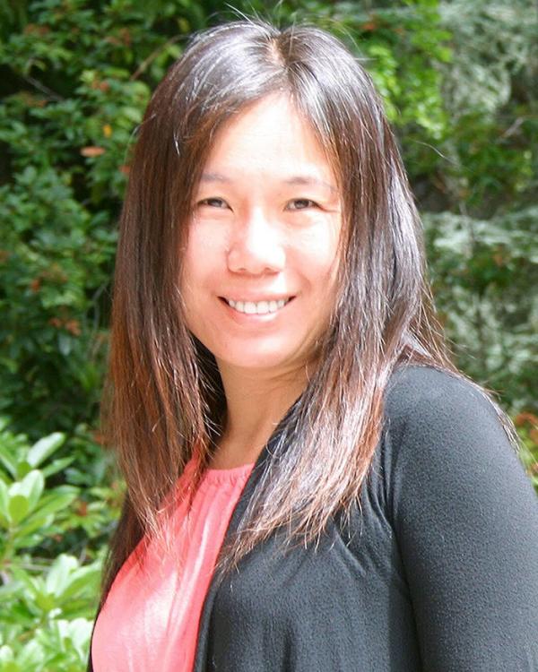 Headshot of Niddy, smiling in front of lush green bushes