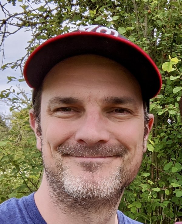 A person is smiling and looking at the camera. He is wearing a hat.