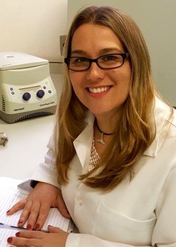 Maria Muller sits at a lab bench with her hands resting on a lab notebook and equipment in the background.