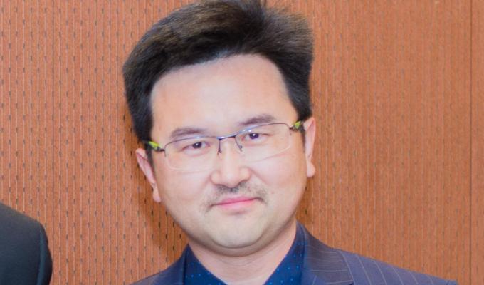 David Xiulei Ji in front of wooden backdrop