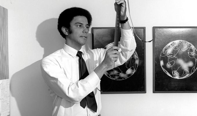 Vintage black and white picture of Warren Washington holding film in office