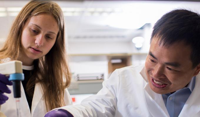 Weihong Qiu pointing at samples with female mentee, Haelyn Epp, in lab