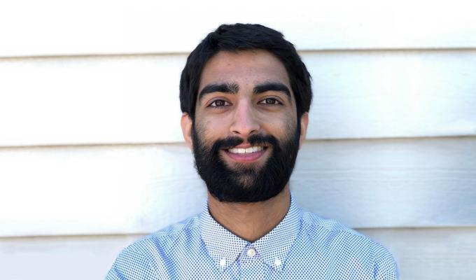 Mahtab Brar smiles in front of a background of white siding.