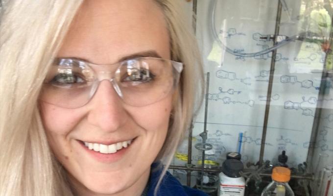 Blonde woman with clear eye protection smiling in a laboratory setting