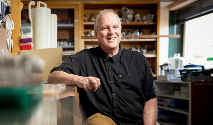 A man sits in a research laboratory with one arm on the benchtop.