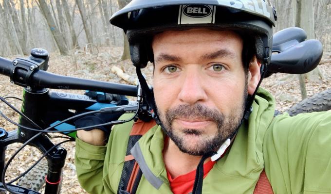 Man wearing a bike helmet and holding a bike
