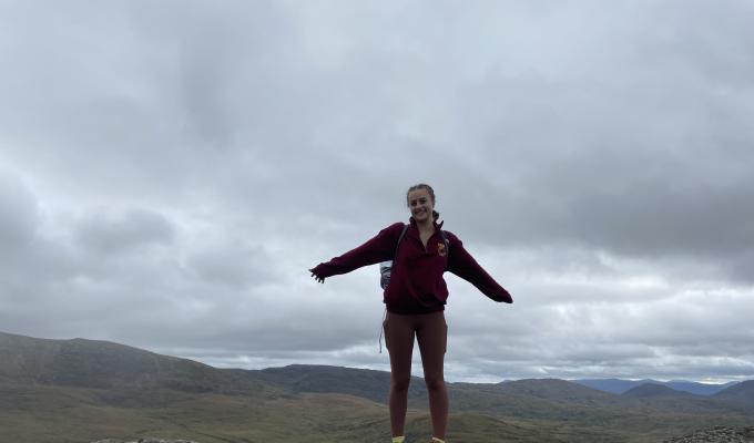 Amelia Noall standing at the top of Torc Mountain in Ireland, overlooking a vast field.