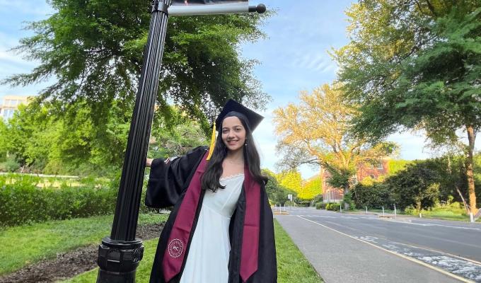 Alyssa Pratt stands in front of a pole with a sign that reads "We did it." She is wearing her graduation cap and gown.