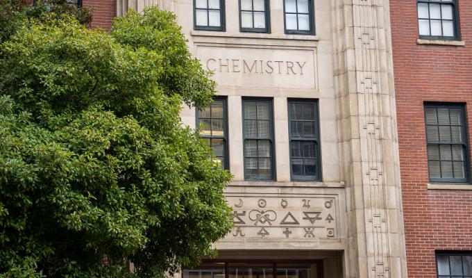 A brick building with the word "chemistry" stands behind a green tree.