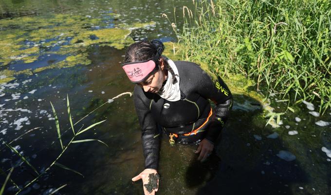 A woman in a stream holds dirt in her hands.