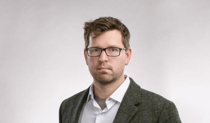 A headshot of a man in a grey suit with white shirt.
