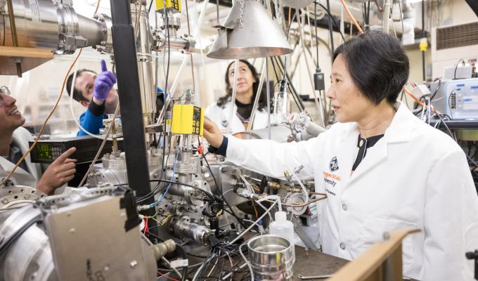 Wei Kong and graduate students work in the lab on a huge machine with wires.