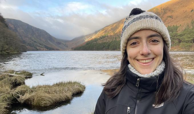 Rachel Sousa stands before a vast body of water at the base of tall, sweeping mountains in Ireland.
