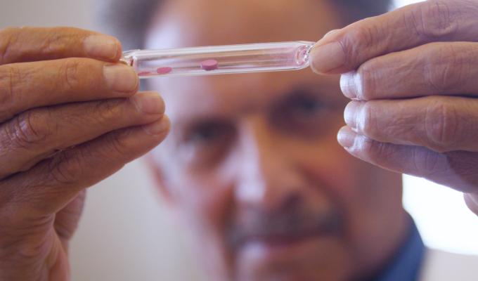 A man in a lab coat holds a vial with a red pigment.