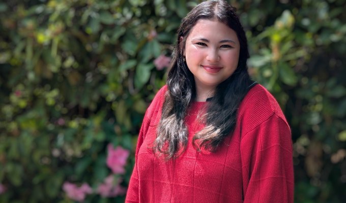 Emily Kaneshiro smiles in front of flowery bushes.