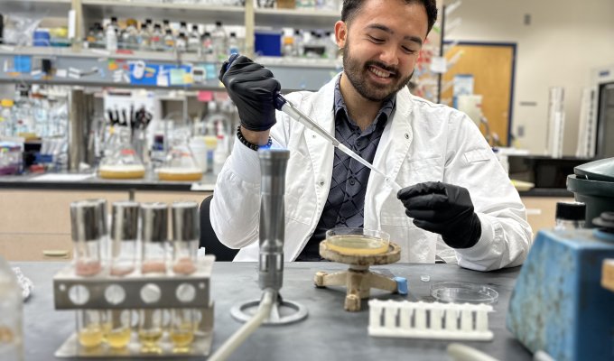 A man in lab coat and gloves uses a pipet.