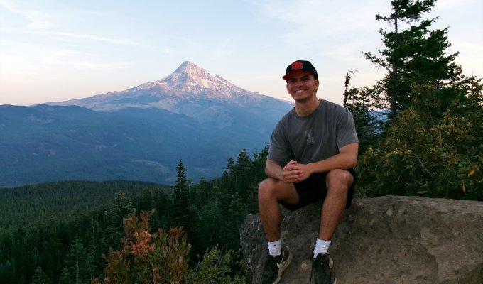 A man poses for a photo with a mountain in the background.