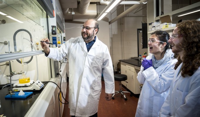 A man in a lab coat works with two students.