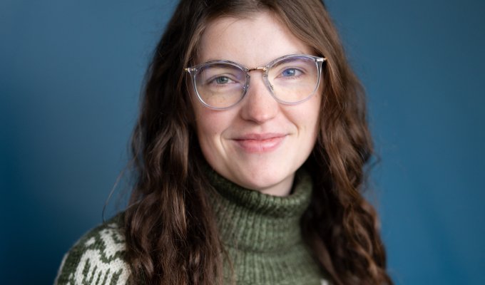 Headshot of a woman in a green fish sweater with long brown hair.
