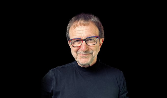 Vincent Racaniello wears a black shirt on a black background and has a playful smile.