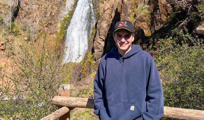 A man stands in front of a waterfall. 