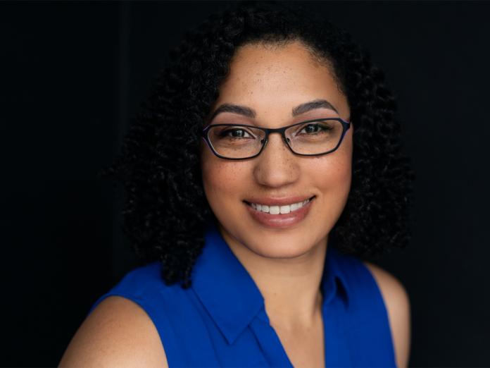 Samantha Lewis in a blue shirt and glasses with dark background