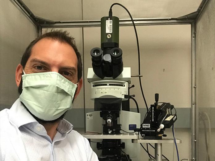 Kenton Hokanson sitting in front of lab equipment with a mask on.