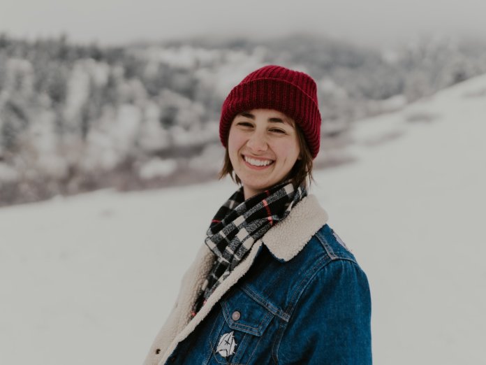 Megan Tucker smiles widely, her scarlet beanie a striking contrast to the snow-covered mountaintops that rise behind her.