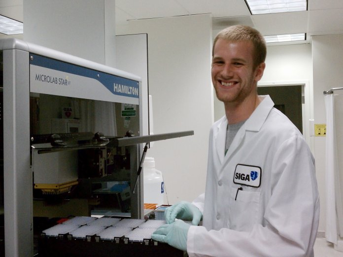 Jonathan Gallion in a lab coat operating an Hamilton Microlab STAR.