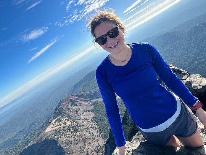 A woman in a blue shirt on top of a mountain.
