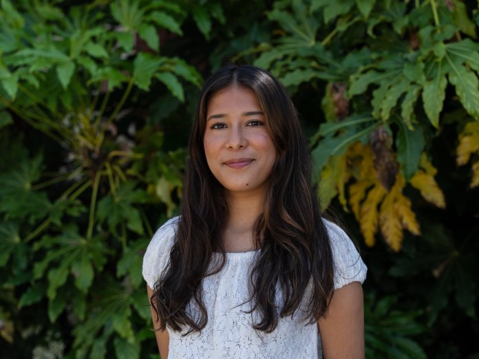 Maria Ruiz Cortes smiles for the camera in front of a green bush.