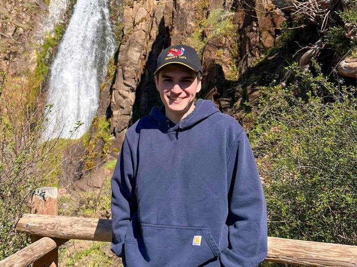 A man stands in front of a waterfall. 