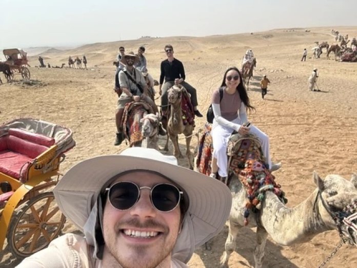 A man in a hat poses while riding a camel.