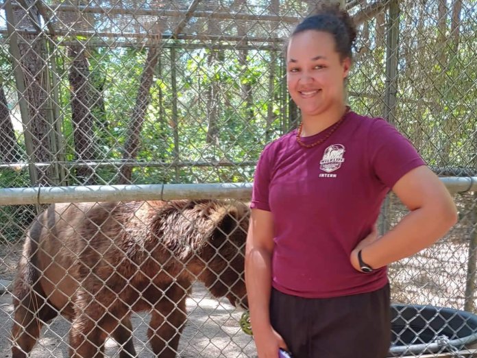 A happy young woman poses with a bear in a wildlife center
